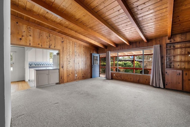 unfurnished living room featuring light colored carpet, wooden ceiling, beam ceiling, and wood walls