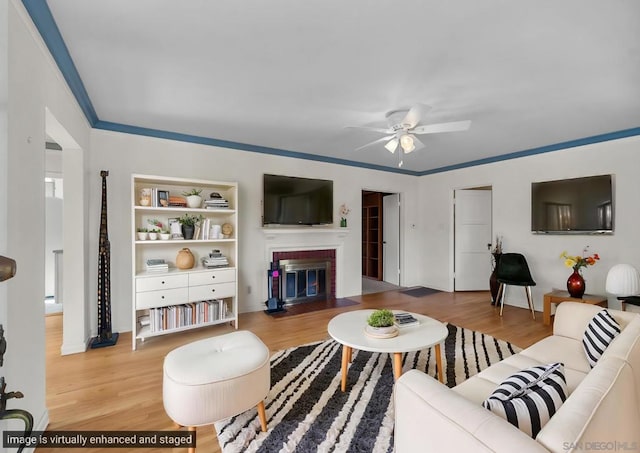 living room with wood-type flooring, a brick fireplace, ornamental molding, and ceiling fan