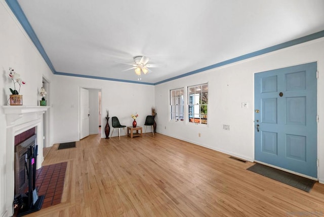 foyer with crown molding, ceiling fan, a fireplace, and light hardwood / wood-style flooring