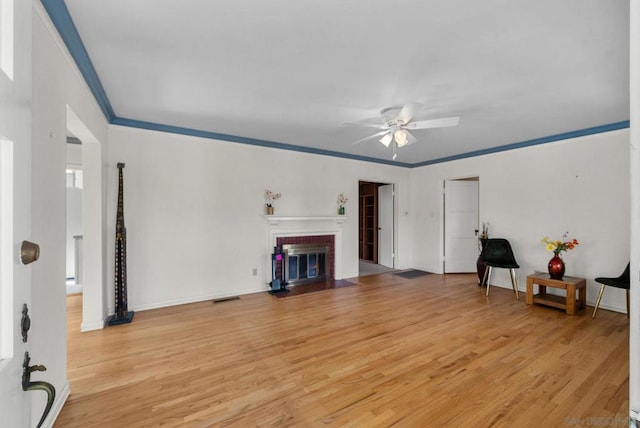 living room featuring a brick fireplace, crown molding, light hardwood / wood-style floors, and ceiling fan