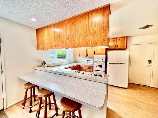 kitchen with white refrigerator, light hardwood / wood-style floors, a kitchen breakfast bar, and kitchen peninsula