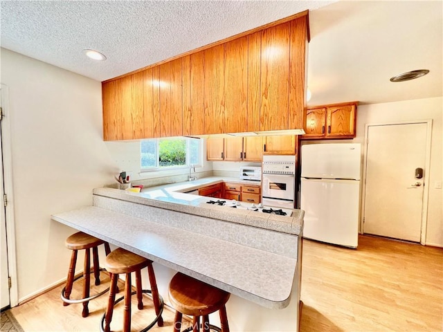 kitchen featuring a peninsula, light wood-style flooring, a kitchen breakfast bar, and freestanding refrigerator