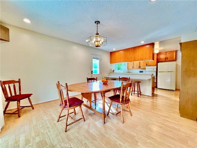 dining area with an inviting chandelier, a textured ceiling, and light wood-type flooring