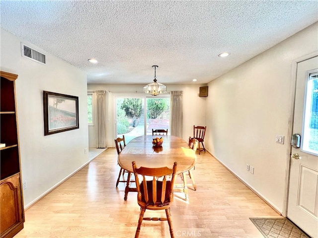 dining area featuring an inviting chandelier, light hardwood / wood-style floors, and a textured ceiling