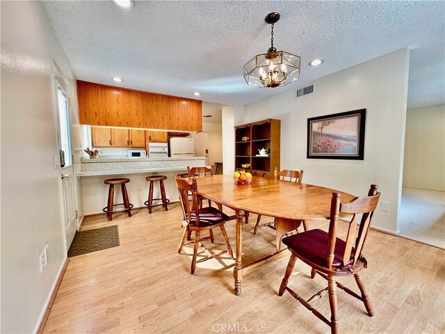 dining room with an inviting chandelier, a textured ceiling, and light hardwood / wood-style floors