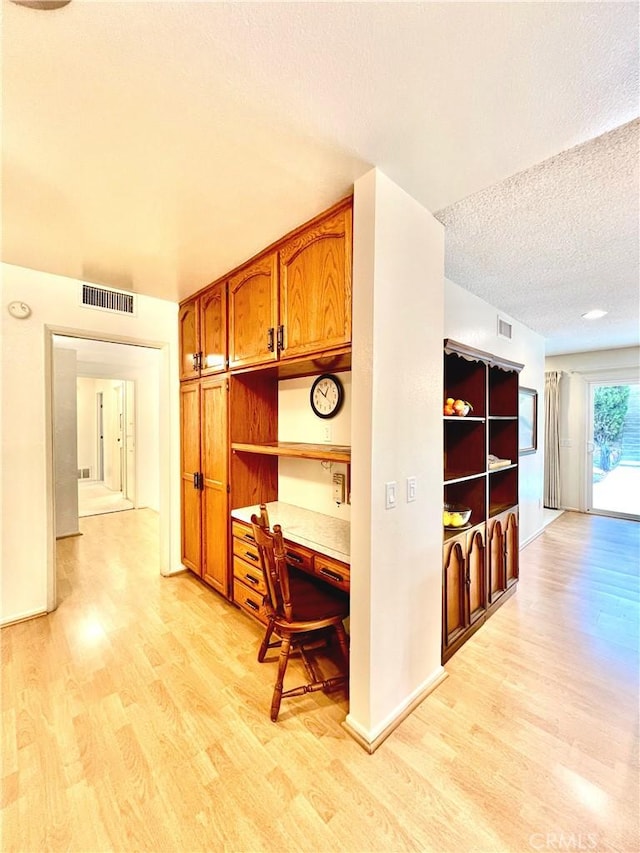 hall with a textured ceiling, light wood-type flooring, visible vents, and baseboards