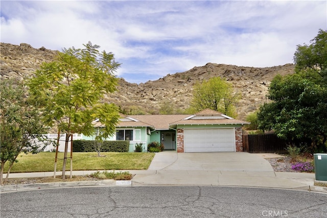 ranch-style house with an attached garage, a mountain view, brick siding, concrete driveway, and a front lawn