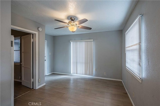 empty room with ceiling fan, a healthy amount of sunlight, wood-type flooring, and a textured ceiling