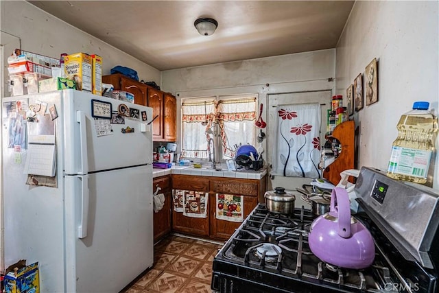 kitchen with sink, tile counters, gas range oven, and white refrigerator