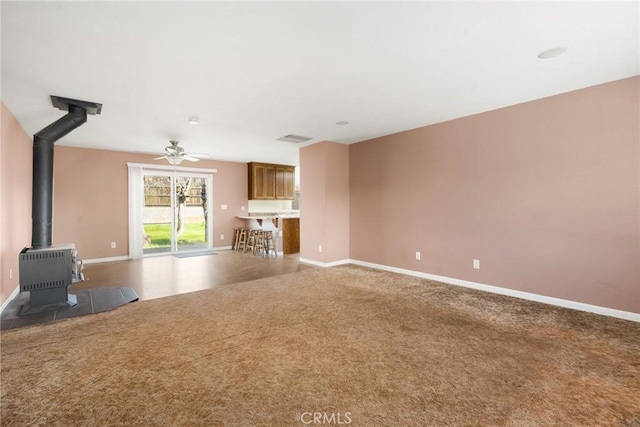 unfurnished living room with a wood stove, ceiling fan, and carpet flooring