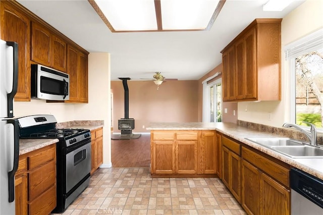 kitchen with sink, ceiling fan, stainless steel appliances, kitchen peninsula, and a wood stove