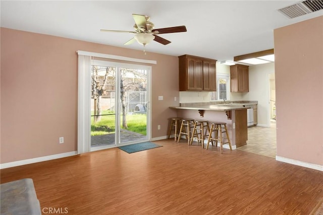 interior space featuring ceiling fan, kitchen peninsula, a breakfast bar area, and light hardwood / wood-style flooring