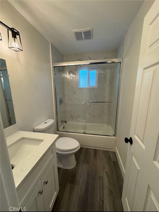 full bathroom with vanity, combined bath / shower with glass door, hardwood / wood-style floors, and toilet