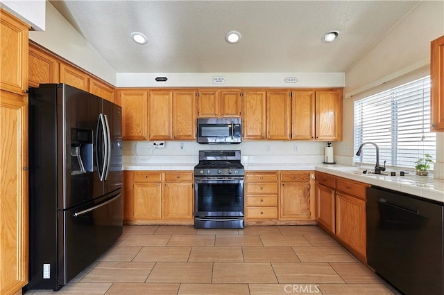 kitchen with lofted ceiling, tile countertops, sink, and black appliances