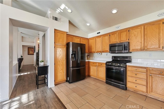 kitchen with tile counters, stainless steel appliances, and vaulted ceiling