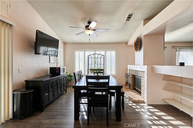 dining area featuring a brick fireplace, dark hardwood / wood-style floors, and ceiling fan