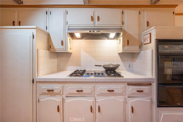 kitchen with tasteful backsplash, white cabinetry, tile countertops, ventilation hood, and oven