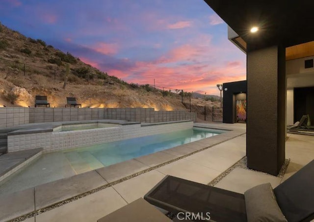 pool at dusk with an in ground hot tub and a patio area