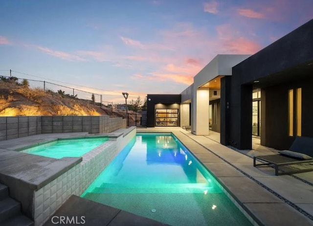 pool at dusk featuring an in ground hot tub