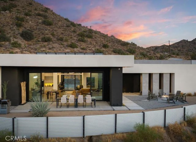 back house at dusk featuring a mountain view and a patio