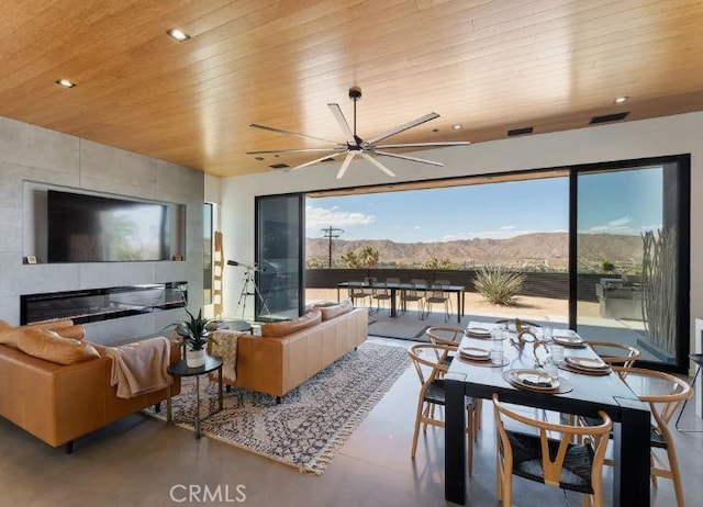 living room with wood ceiling, ceiling fan, concrete flooring, a tiled fireplace, and a mountain view