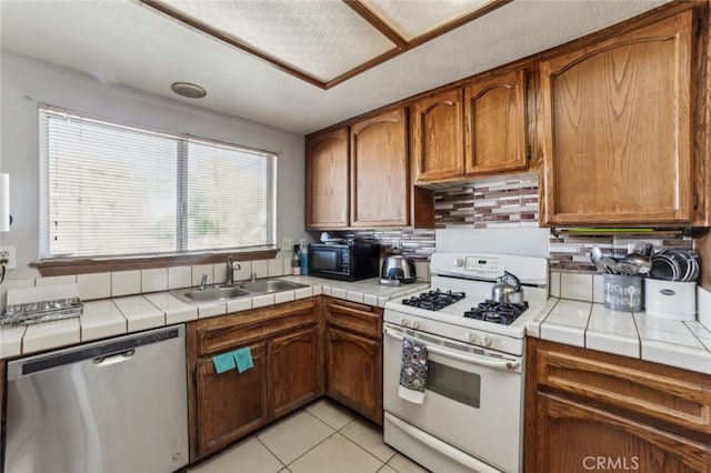 kitchen featuring light tile patterned floors, sink, dishwasher, tile counters, and white gas range