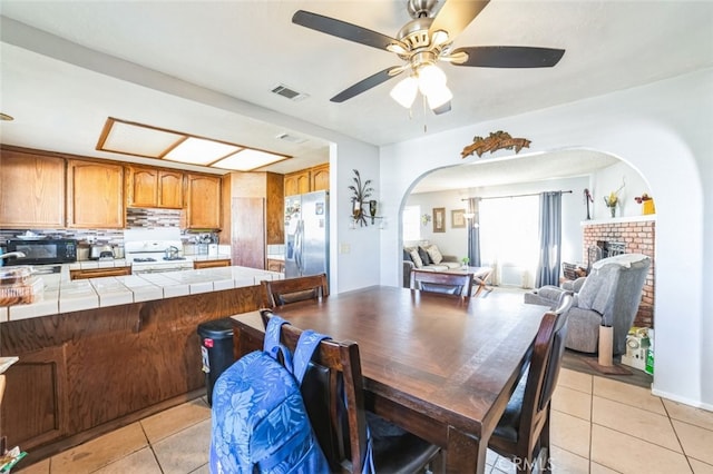 dining area featuring light tile patterned flooring, ceiling fan, and a brick fireplace