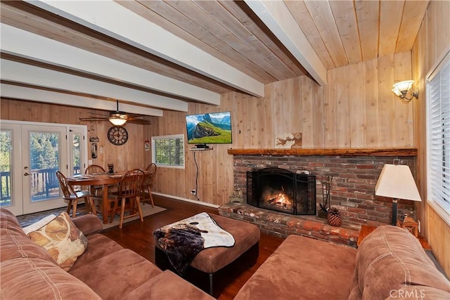 living room featuring beamed ceiling, a fireplace, wooden walls, and wood finished floors