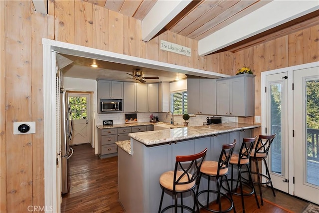 kitchen featuring appliances with stainless steel finishes, gray cabinetry, a kitchen bar, and kitchen peninsula