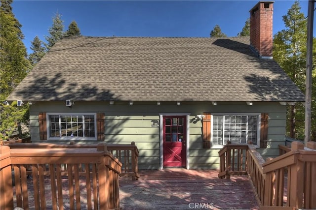 back of house with a chimney, roof with shingles, and a wooden deck