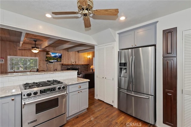 kitchen with gray cabinetry, stainless steel appliances, light stone countertops, beamed ceiling, and wood walls