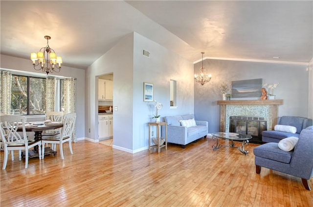 living room with vaulted ceiling, a fireplace, an inviting chandelier, and light hardwood / wood-style floors