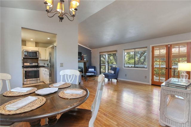 dining space with a notable chandelier, vaulted ceiling, french doors, and light wood-type flooring