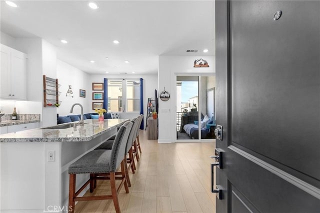 kitchen featuring white cabinetry, an island with sink, sink, a kitchen bar, and light hardwood / wood-style flooring