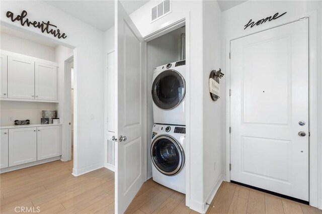 laundry room featuring stacked washer / drying machine and light hardwood / wood-style flooring