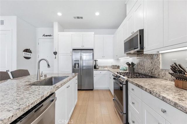 kitchen with white cabinetry, appliances with stainless steel finishes, light stone countertops, and sink