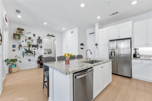 kitchen featuring stainless steel appliances, white cabinetry, sink, and a kitchen island with sink