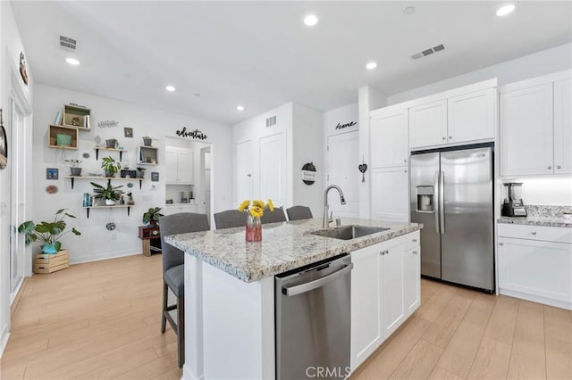 kitchen with stainless steel appliances, white cabinets, a sink, and a center island with sink