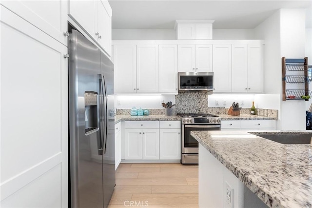 kitchen featuring light hardwood / wood-style flooring, stainless steel appliances, light stone countertops, decorative backsplash, and white cabinets