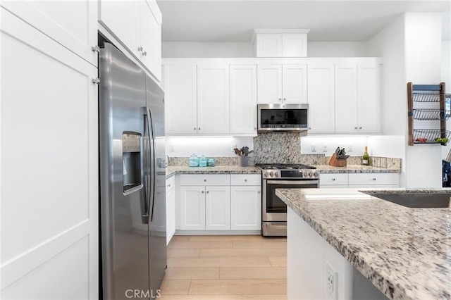 kitchen with light wood-style flooring, light stone countertops, stainless steel appliances, white cabinetry, and decorative backsplash