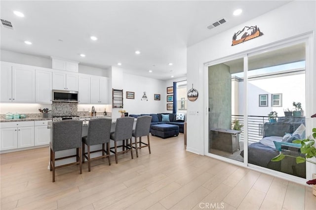 kitchen featuring white cabinetry, a breakfast bar area, backsplash, light stone countertops, and light wood-type flooring