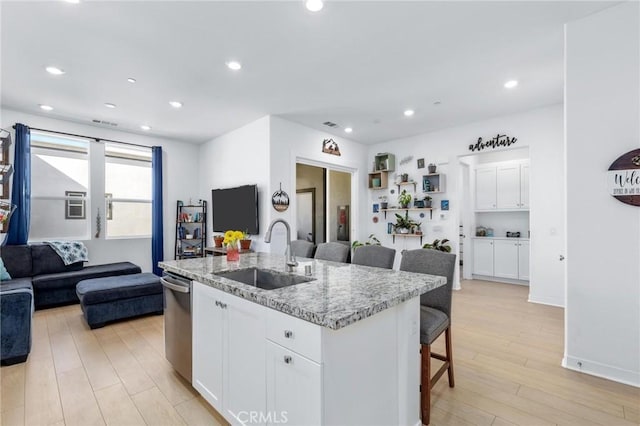 kitchen with sink, a breakfast bar, a kitchen island with sink, white cabinets, and stainless steel dishwasher