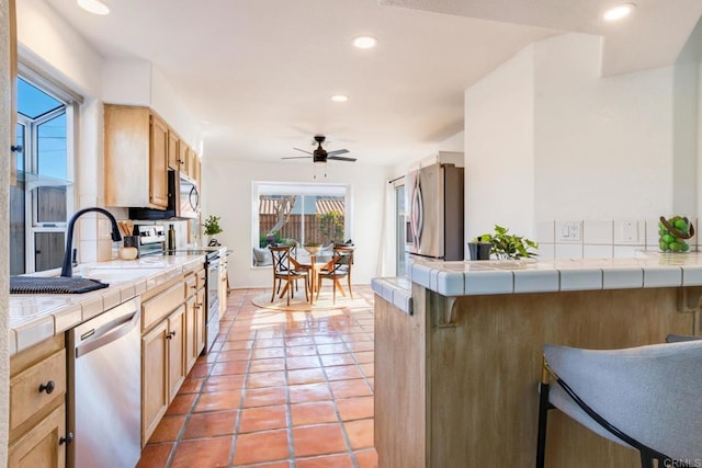 kitchen with light tile patterned floors, ceiling fan, stainless steel appliances, light brown cabinetry, and tile countertops