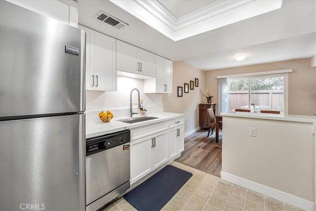 kitchen featuring sink, white cabinetry, crown molding, appliances with stainless steel finishes, and a raised ceiling