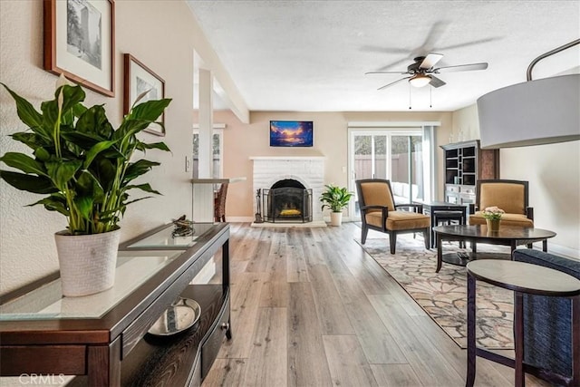 living room with a fireplace, a textured ceiling, light hardwood / wood-style flooring, and ceiling fan