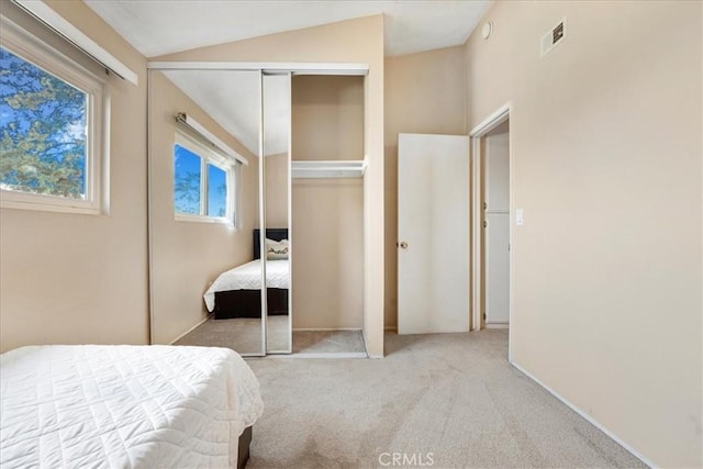 bedroom with vaulted ceiling, light colored carpet, and a closet