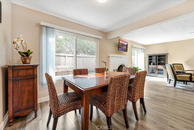 dining area with a fireplace, a wealth of natural light, beamed ceiling, and light wood-type flooring