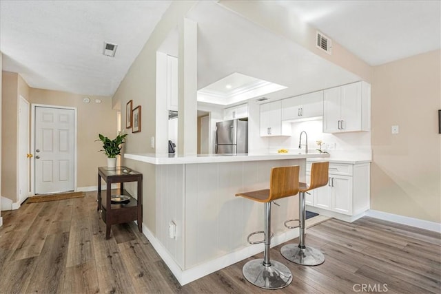 kitchen featuring dark wood-type flooring, a kitchen bar, white cabinetry, stainless steel fridge, and kitchen peninsula