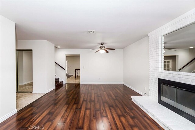 unfurnished living room with dark hardwood / wood-style flooring, a brick fireplace, and ceiling fan