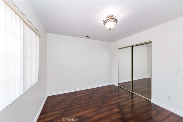 unfurnished bedroom featuring a closet, wood finished floors, visible vents, and baseboards